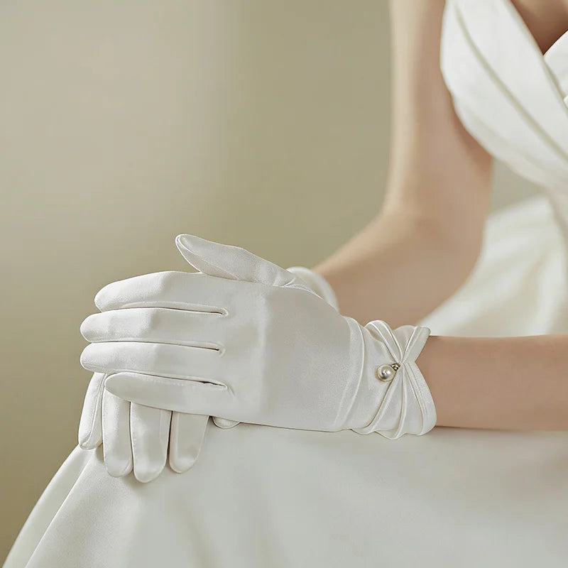 Gants femme en satin blanc portés, mains posées sur une robe de mariée